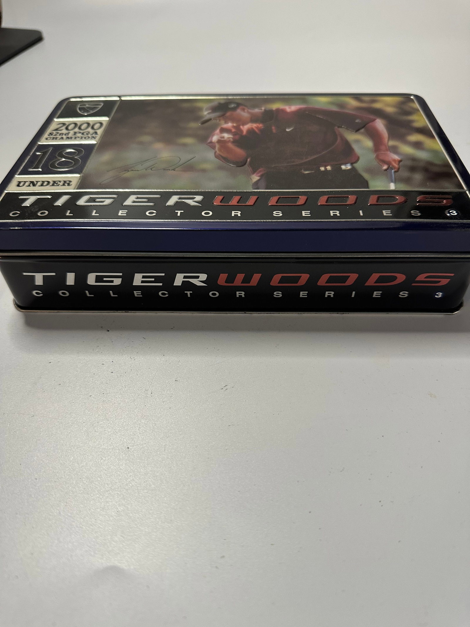 2000 Tiger Woods Collector Series 3 Tin: This is a collectible metal tin featuring Tiger Woods. It is labeled as the Collector Series 3 and highlights his 2000 82nd PGA Championship win. The tin features imagery of the athlete along with