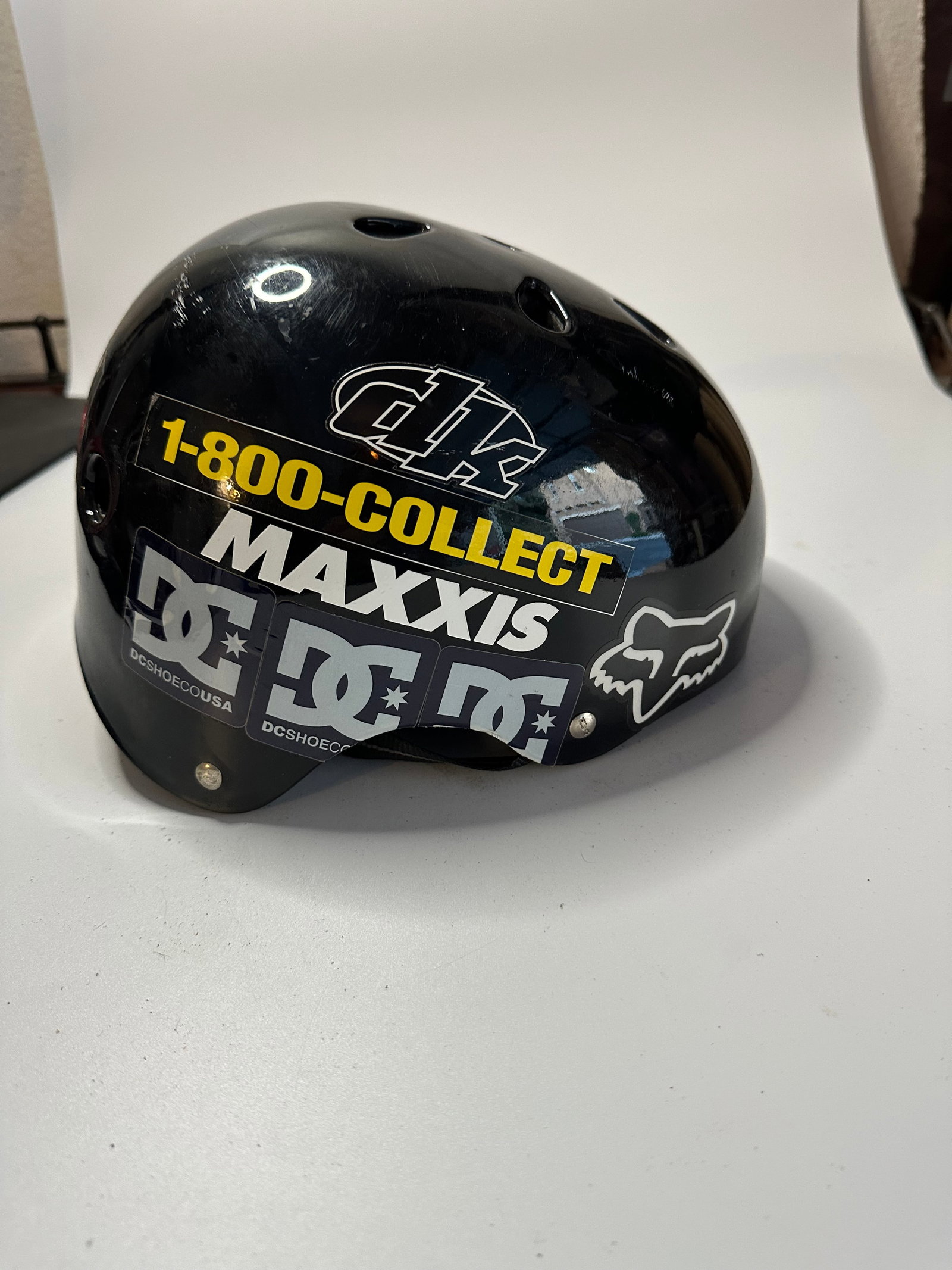 Fox Racing Sports Helmet: This is a black Fox Racing sports helmet adorned with various brand stickers including 1-800-COLLECT, Maxxis, and DC Shoes. The helmet features a glossy finish and shows signs of use with several