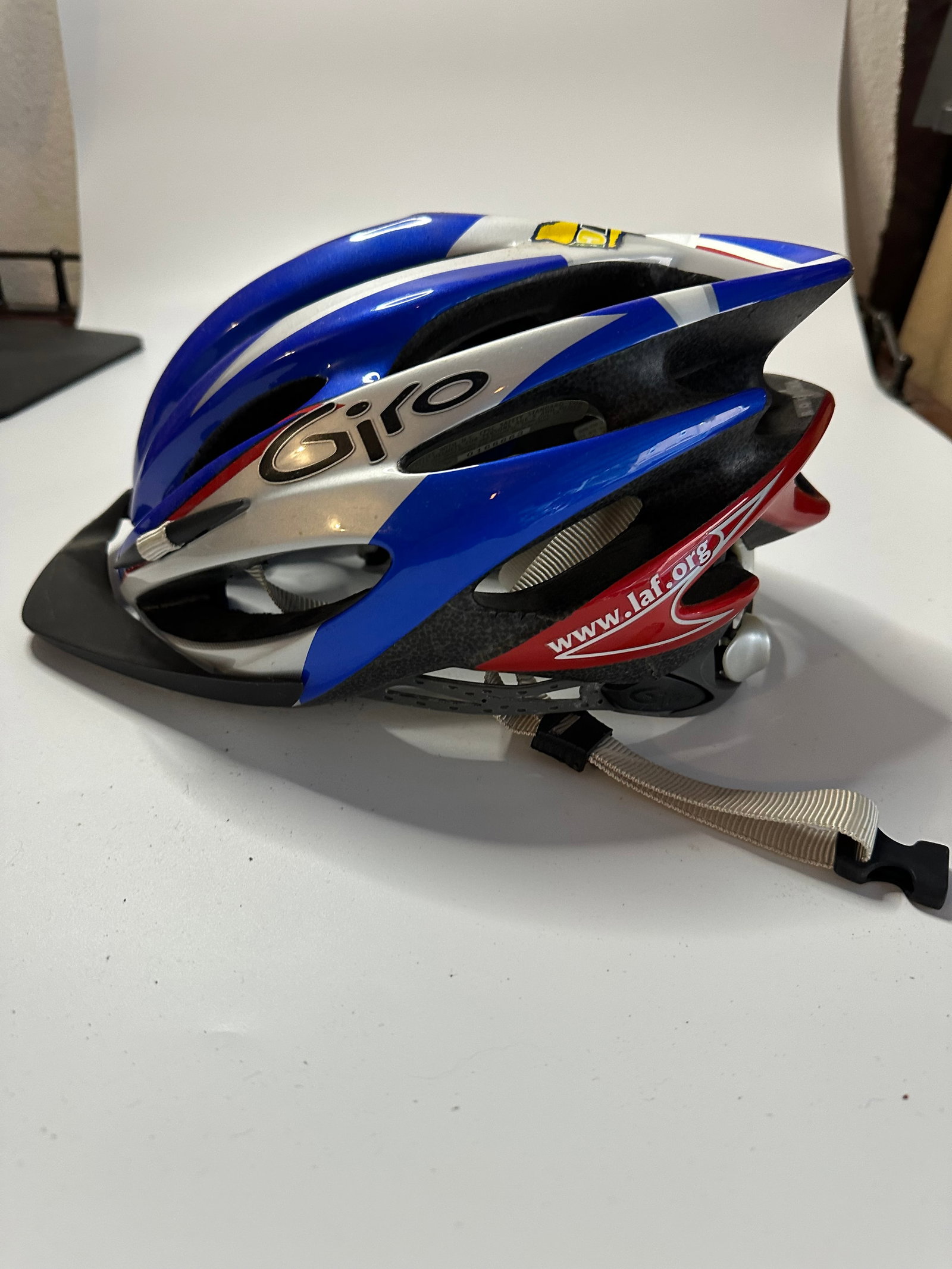 Giro Bicycle Helmet: This is a Giro branded bicycle helmet featuring a red, white, and blue color scheme. The helmet includes branding text indicating 'www.laf.org' along the side. It is a ventilated design with an