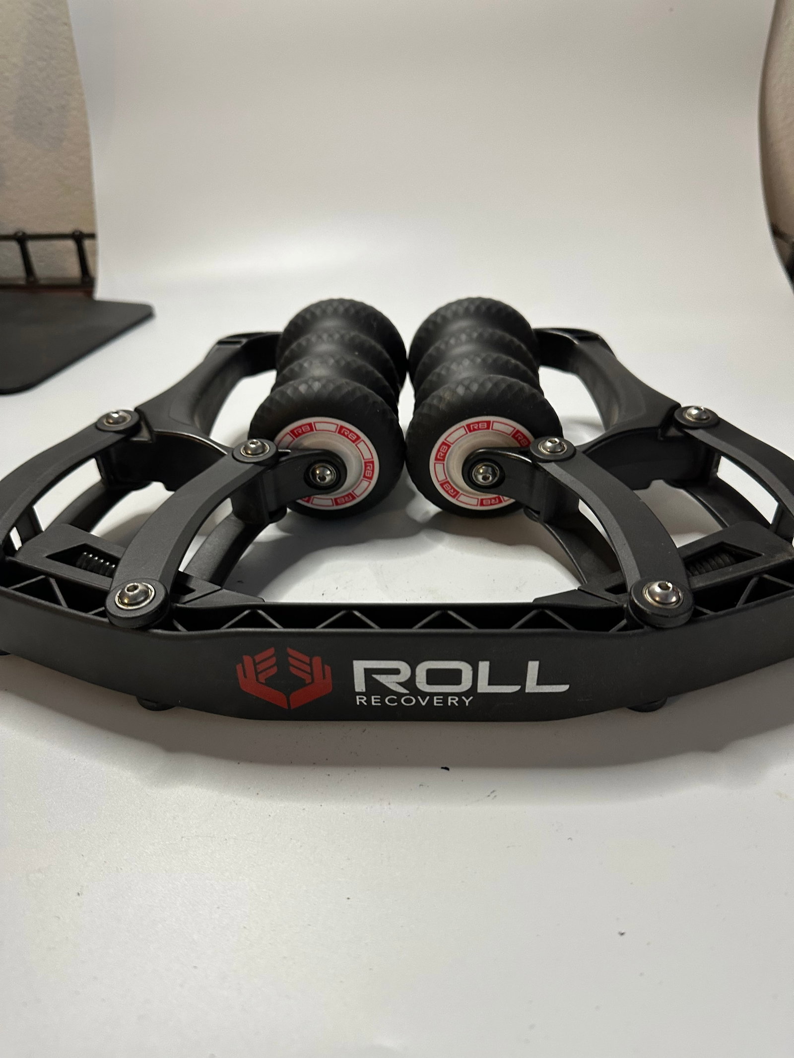 Roll Recovery R8: This is a black Roll Recovery R8 massage tool designed for deep tissue muscle therapy. It features multiple rolling wheels with the RR brand logo clearly printed on the center of the wheels and along