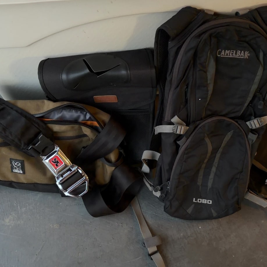 Chrome and Camelbak Bags Lot: This lot features a collection of bags, including a brown Chrome messenger bag with a distinctive seatbelt-style buckle and a black Camelbak Lobo hydration backpack. The items appear to be in pre-owne