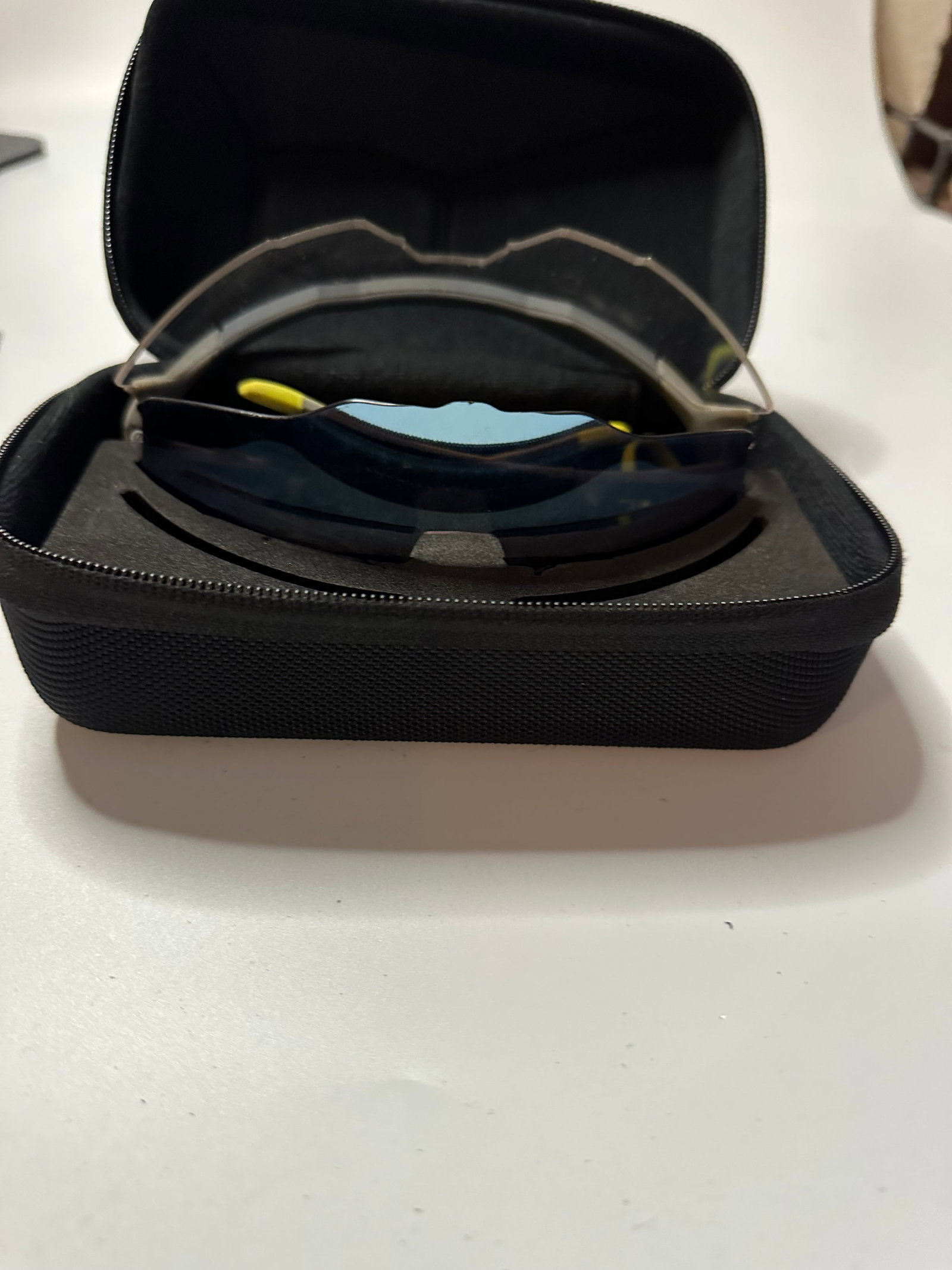 Sport Performance Sunglasses with Hard Case: This item features a pair of sport performance sunglasses with dark, reflective lenses housed inside a protective black zippered hard case. The sunglasses appear to have a sleek, wraparound design
