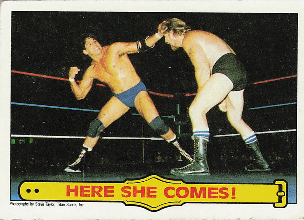 1985 Topps WWF Pro Wrestling Stars "Here She Comes!" #28 trading card: The 1985 Topps WWF Pro Wrestling Stars "Here She Comes!" #28 trading card frames an in-ring action photograph of WWE Hall of Famer Tito Santana battling journeyman competitor Steve Taylor. Modeled