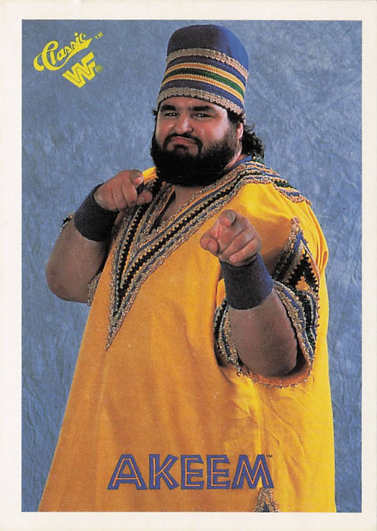 1990 Classic WWF Akeem #25 trading card: The 1990 Classic WWF Akeem #25 trading card features a blue, crumpled-texture border framing a portrait photograph of the larger-than-life wrestler smiling and pointing at the viewer while wearing