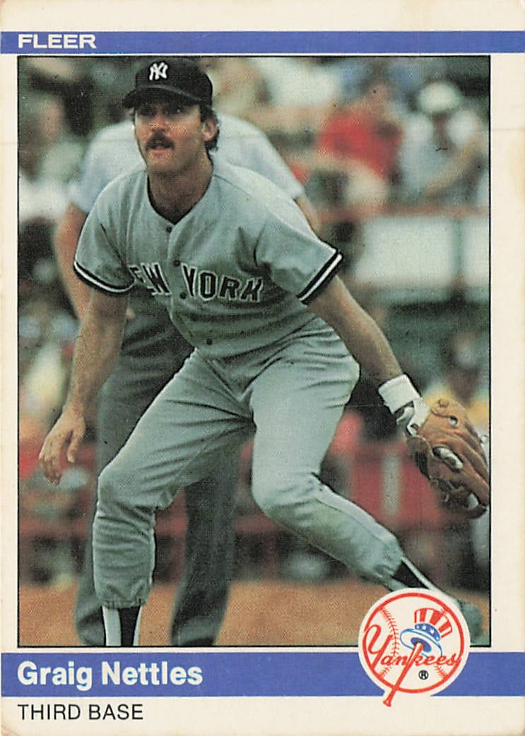 1984 Fleer Graig Nettles New York Yankees #135: The 1984 Fleer Graig Nettles New York Yankees #135 baseball card depicts the elite defensive third baseman in a classic low-set fielding stance on the diamond. Adhering to the standard 1984 Fleer