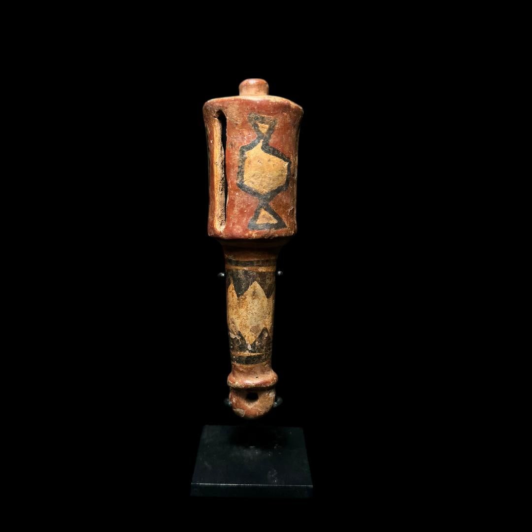Pre-Columbian Chiribaya Painted Pottery Rattle, Peru: A Pre-Columbian Chiribaya painted pottery rattle from Peru, of elongated cylindrical form with a bulbous upper chamber and slit openings designed to produce sound. The surface is decorated in earthy r