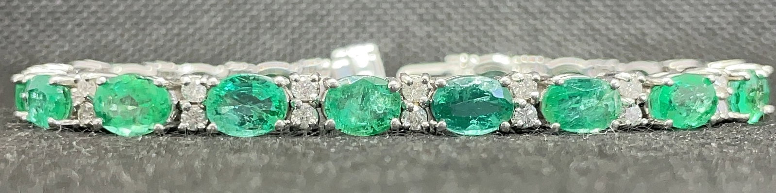 14k White Gold 13.00ctw Oval Emerald & 1.00ctw Diamond Bracelet (17.7g): Indulge in the vibrant luxury of this emerald and diamond statement bracelet. Masterfully handcrafted in 14k white gold, the piece features 13.00 carats total weight of oval-cut emeralds paired with 1