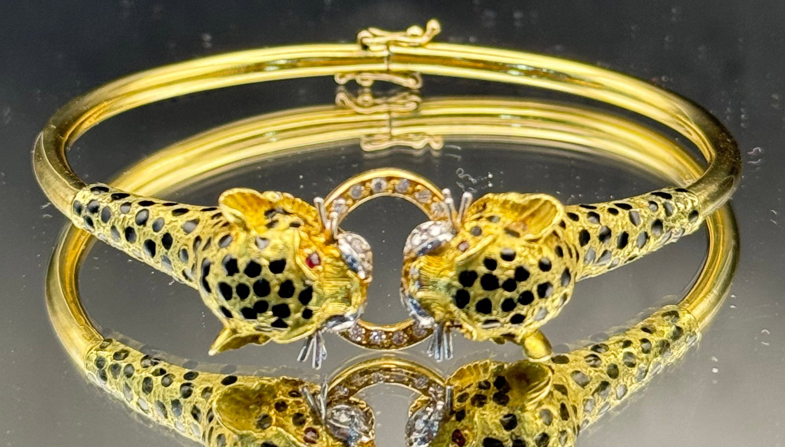 VINTAGE 1980s 18K GOLD LEOPARD BANGLE WITH DIAMONDS & RUBIES: Wonderful 1980s vintage bangle depicting two leopards biting the same diamond ring. This exceptional treasure is crafted in 18K yellow gold and decorated with intricate black enamel spots. Both leopar