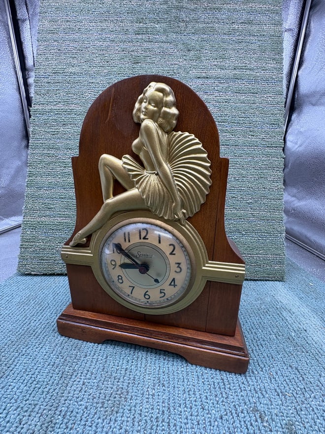 Vintage Sessions Art Deco Mantel Clock – Figural Flapper Lady – Wood Case: Vintage Sessions mantel clock featuring a striking Art Deco-style flapper figure seated above the clock face. The figure is rendered in a gold-tone finish with stylized hair and drapery, typical of 19