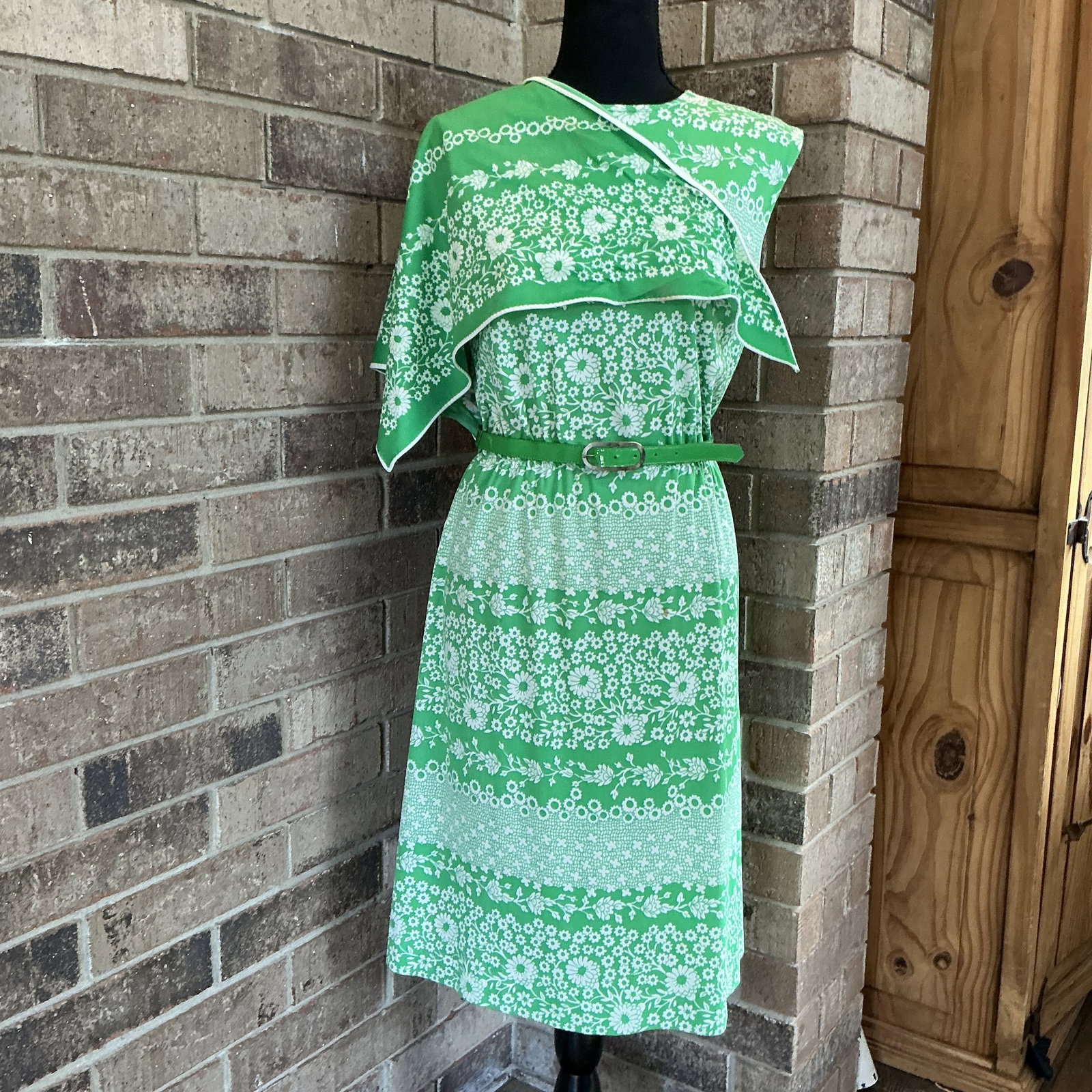 Vintage R&K Knits Green Floral Dress with Cape Overlay & Belt: Charming vintage R&K Knits dress featuring a vibrant green and white floral pattern throughout. This eye-catching piece includes a unique cape-style overlay across the shoulders, adding movement and a