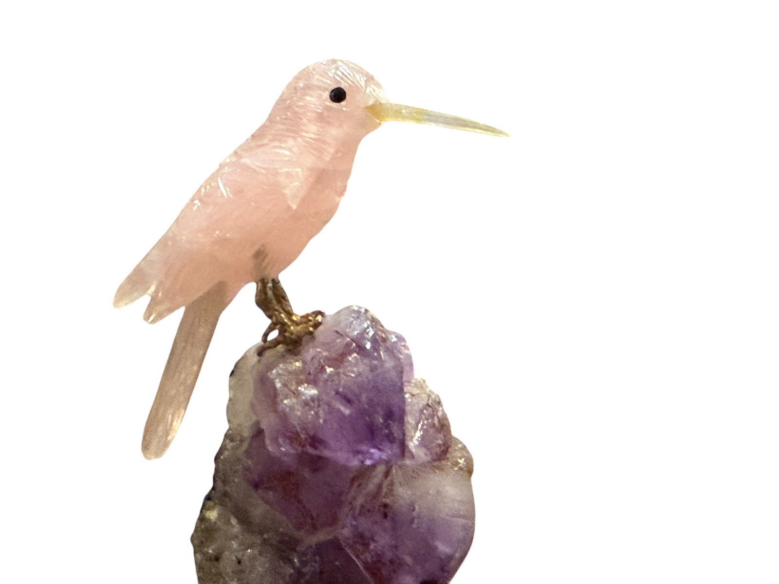 Carved Rose Quartz Bird on Amethyst Crystal Sculpture: Carved Rose Quartz Bird on Amethyst CrystalA decorative carved stone bird, likely rose quartz, perched on a natural amethyst crystal base. The figure features detailed feather carving and a long beak,
