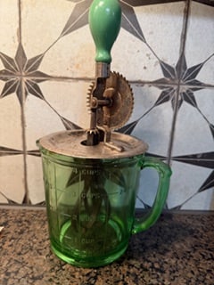 Depression-Era Green Glass Hand-Crank Batter Mixer Measuring Cup, c. 1930s: Vintage Depression-era emerald green glass hand-crank batter mixer featuring an integrated measuring cup with embossed graduations for cups, pints, and ounces. The mixer is fitted with its original me
