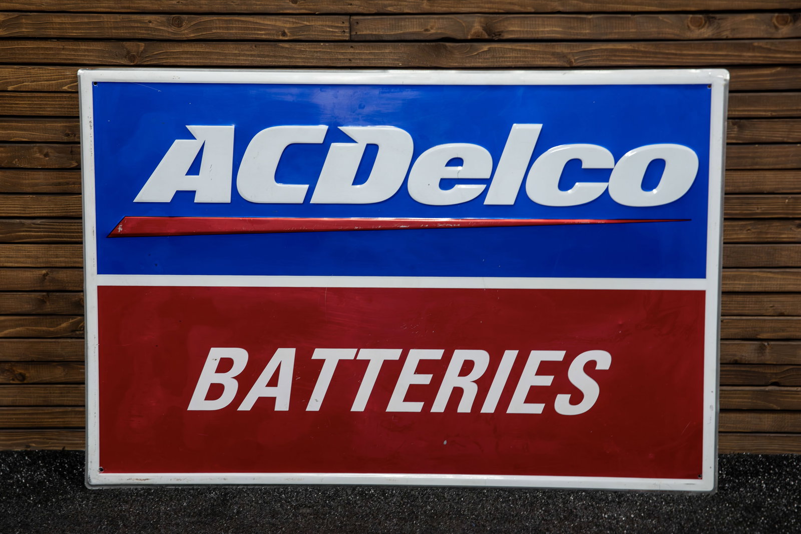 AC Delco Batteries Embossed Tin Sign: Features white letters against blue field for company name and product also with white letters against a maroon field, raised outer border, light surface wear with excellent preservation of colors