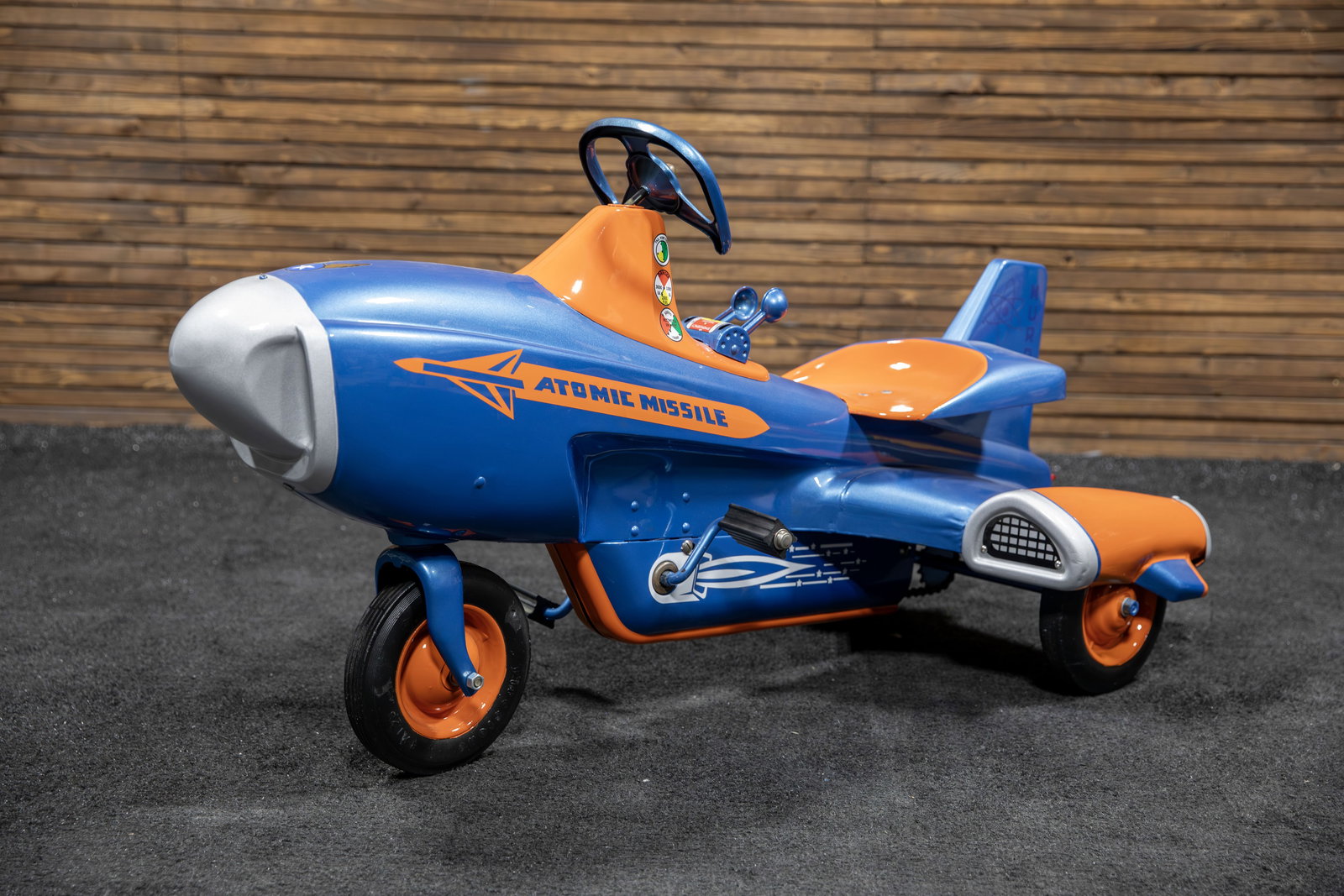 Atomic Missile Pedal Car: Colorful professional restoration with paint in blue metallic and orange, authentic graphics, dual missile control levers, Firestone black rubber tires, chain drive, red jeweled reflectors, a truly