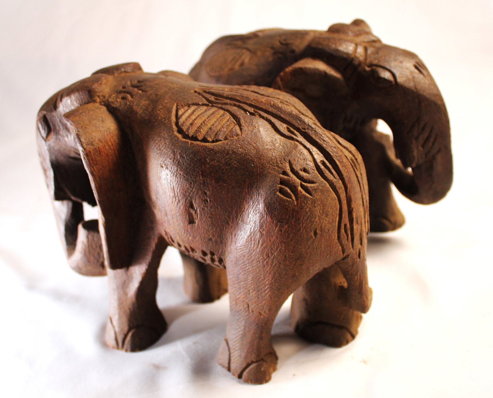 EAST AFRICAN ELEPHANTS: This pair of hand-carved elephant sculptures is crafted from a dense, heavy tropical hardwood, displaying a rich, naturally aged dark brown patina. The figures feature prominent, deep-grain