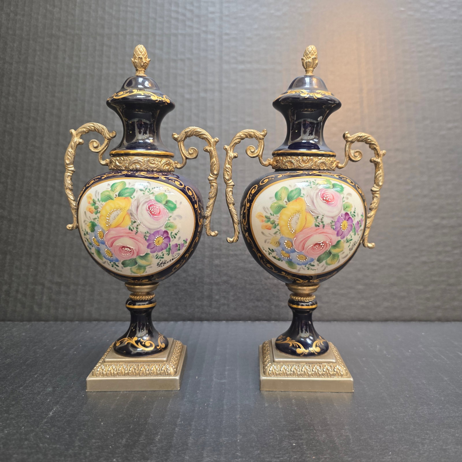 A Pair of Cobalt Blue Porcelain Hand Painted Sevres French Decorative Urn By ACF: A pair of ACF Sèvres style cobalt blue porcelain urn vases with hand-painted floral motifs and gilded bronze mounts. The vases feature a deep cobalt blue porcelain body, decorated with hand-painted