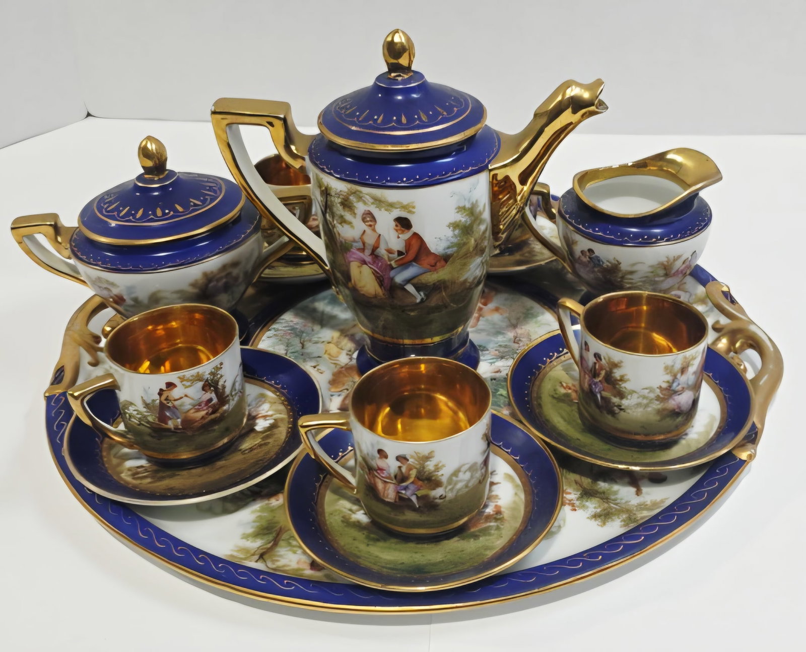 Royal Austria Porcelain Tea Set: This dainty Tea set is in the Royal Vienna style, a category of porcelain highly sought after for its opulent neoclassical and romantic aesthetic. The set features deep cobalt blue bands with heavy