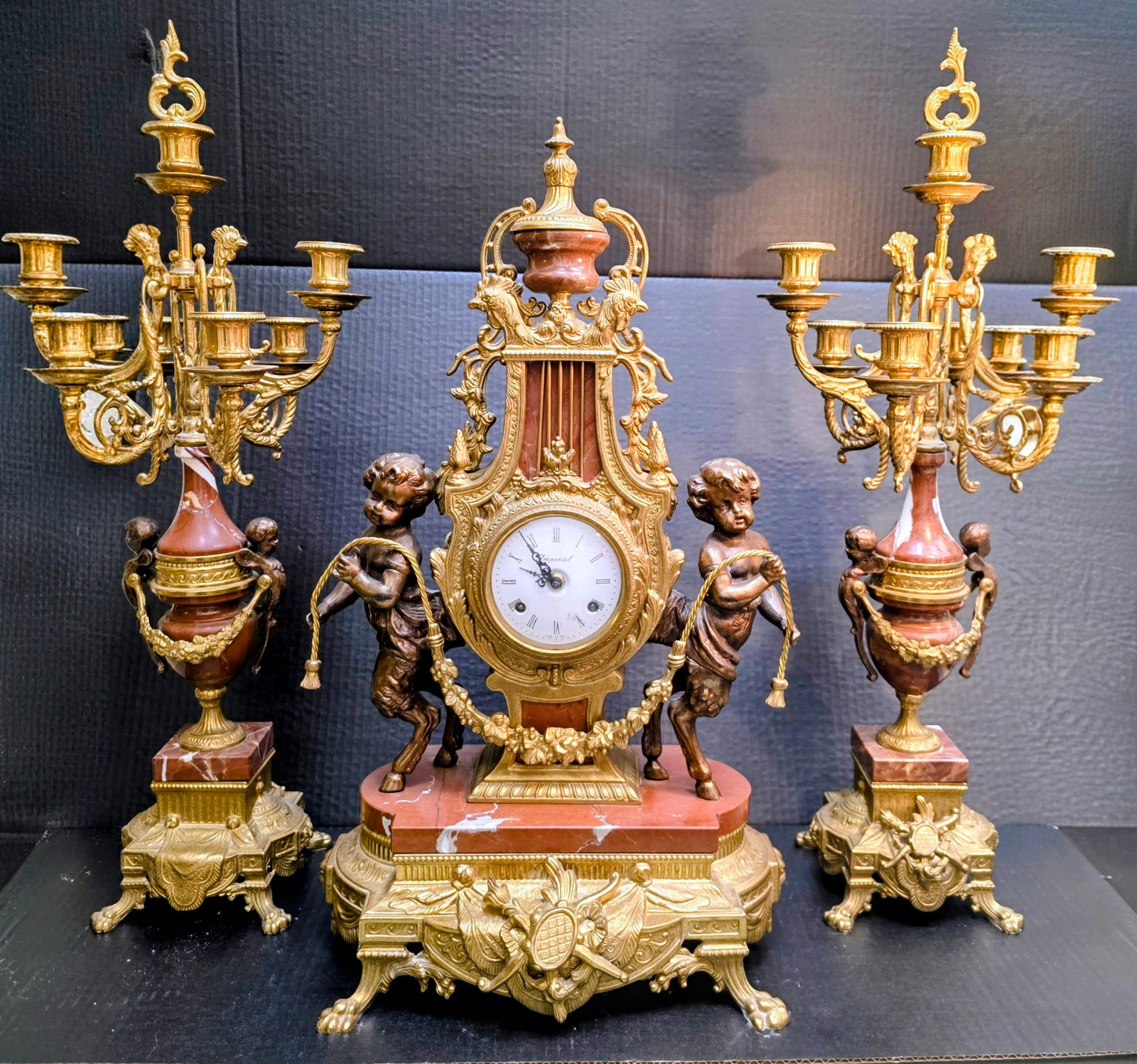 Ornate Gilt Bronze and Rouge Griotte Marble Candleabra Garniture Set Italian: Brevettato Imperial mantel clock, featuring Pan with a matching pair of candleabras featuring cherubs. The clock chimed and ticked when wound a bit.