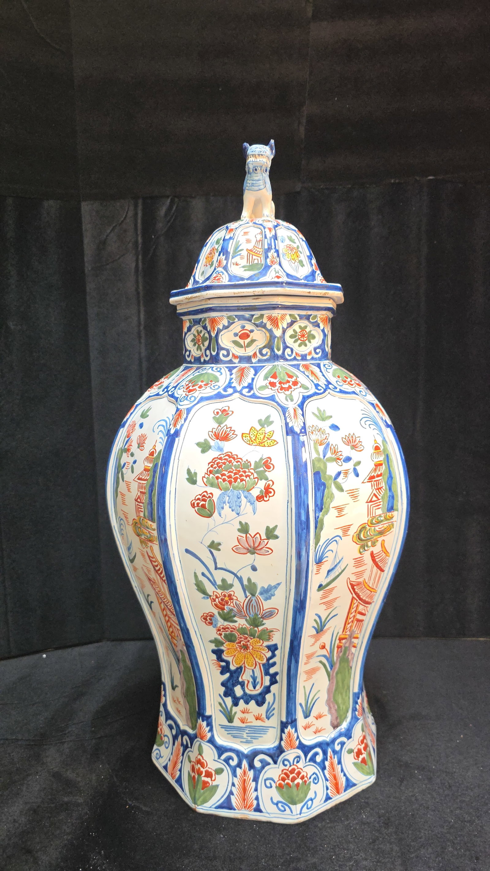 Delftware Polychrome Vase: A 24" tall vibrant Delftware polychrome vase The lid has a Foo dog Finial in Chinoiserie fashion. There are minor imperfections and chips at base