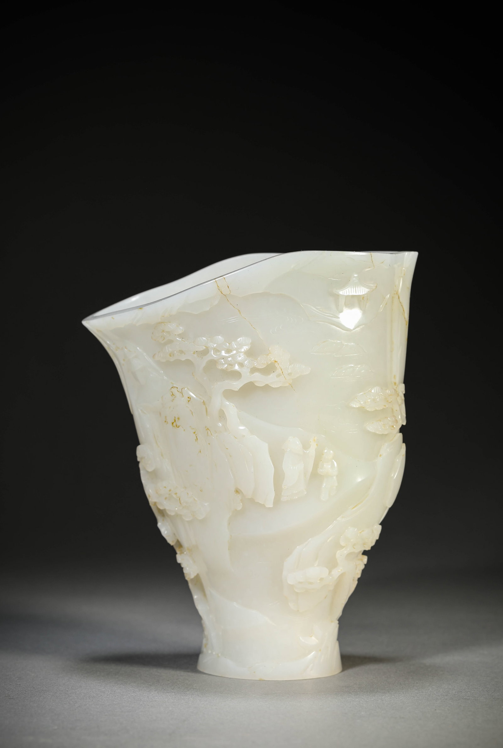 A CARVED JADE 'SCHOLARS UNDER PINE TREE' CUP: A CARVED JADE 'SCHOLARS UNDER PINE TREE' CUP Length: 13.1 cm (5.2 in.), Width: 8.3 cm (3.3 in.), Height: 15.8 cm (6.2 in.). All measurements are approximate.
