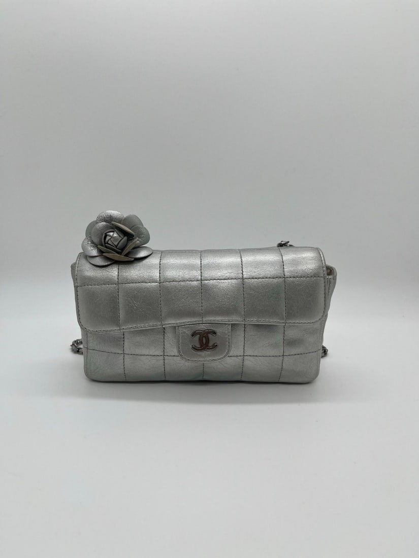 CHANEL Camellia Chocolate Bar Flap Bag Silver Metallic Lambskin Chain: Condition: Normal signs of wear. Logo is worn out. Shoulder strap buckle has damage. Bag buckle shows obvious wear. There are yellow stains on the petal part on the left side of the bag, as well as in
