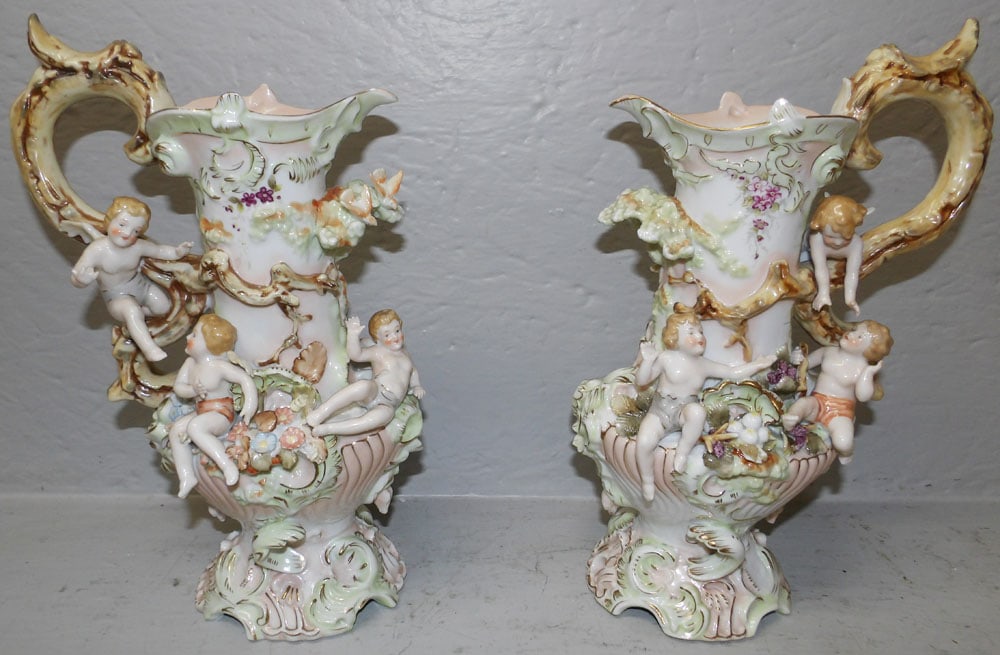 Pair of German Style Porcelain Figural Ewers with Cupid Motif, (One As Is): Pair of German Style Porcelain Figural Ewers with Cupid Motif, (One As Is). 12 1/4" H 7 1/2" W ALL DESCRIPTIONS AND ANY CONDITION STATEMENT GIVEN BY LANGSTON AUCTION GALLERY ARE STRICTLY OPINIONS