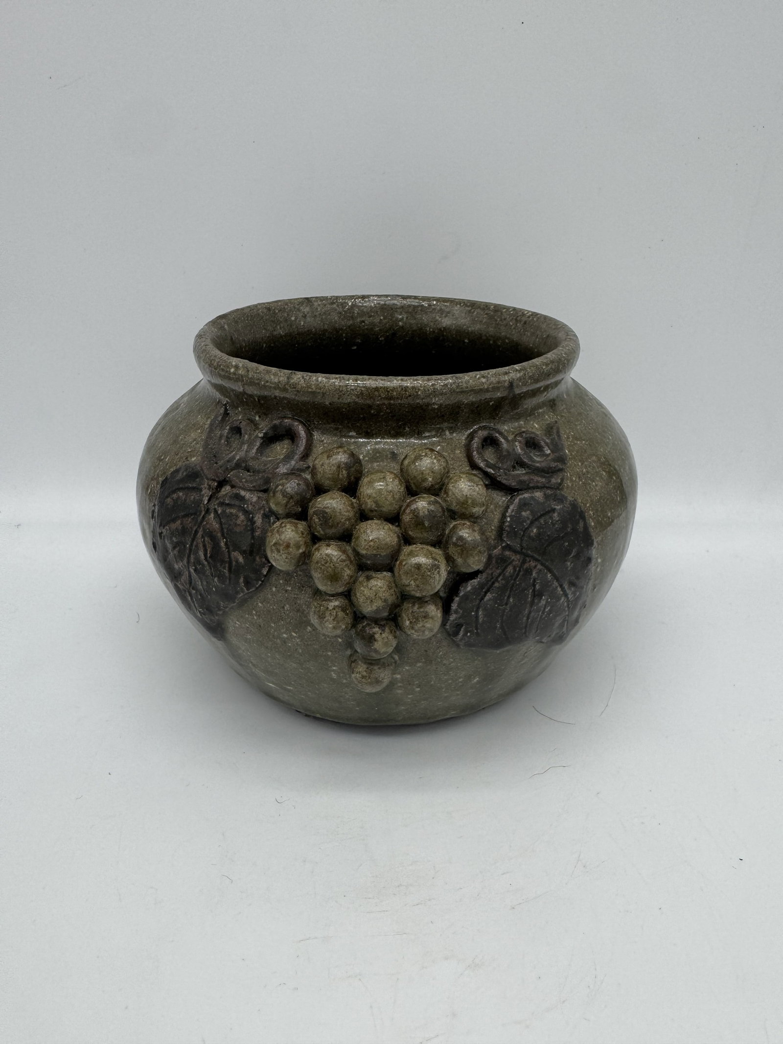 Arie Meaders Decorated Pot: A beautiful decorated pot by Arie Meaders, featuring applied grape clusters and leaf designs on both sides of the form. The grapes are finished in the same glaze as the body, while the leaves are