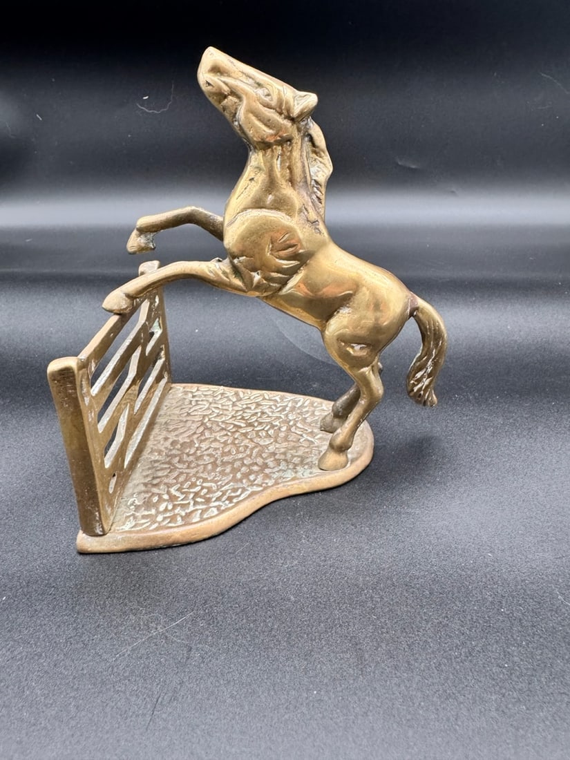 Vintage English Brass Horse Jumping Fence Bookend: Mid 20th Century: This item is a vintage English brass horse bookend depicting a horse jumping over a fence. The material is a solid brass with a mellowed patina. This bookend was popular in the mid-20th century,
