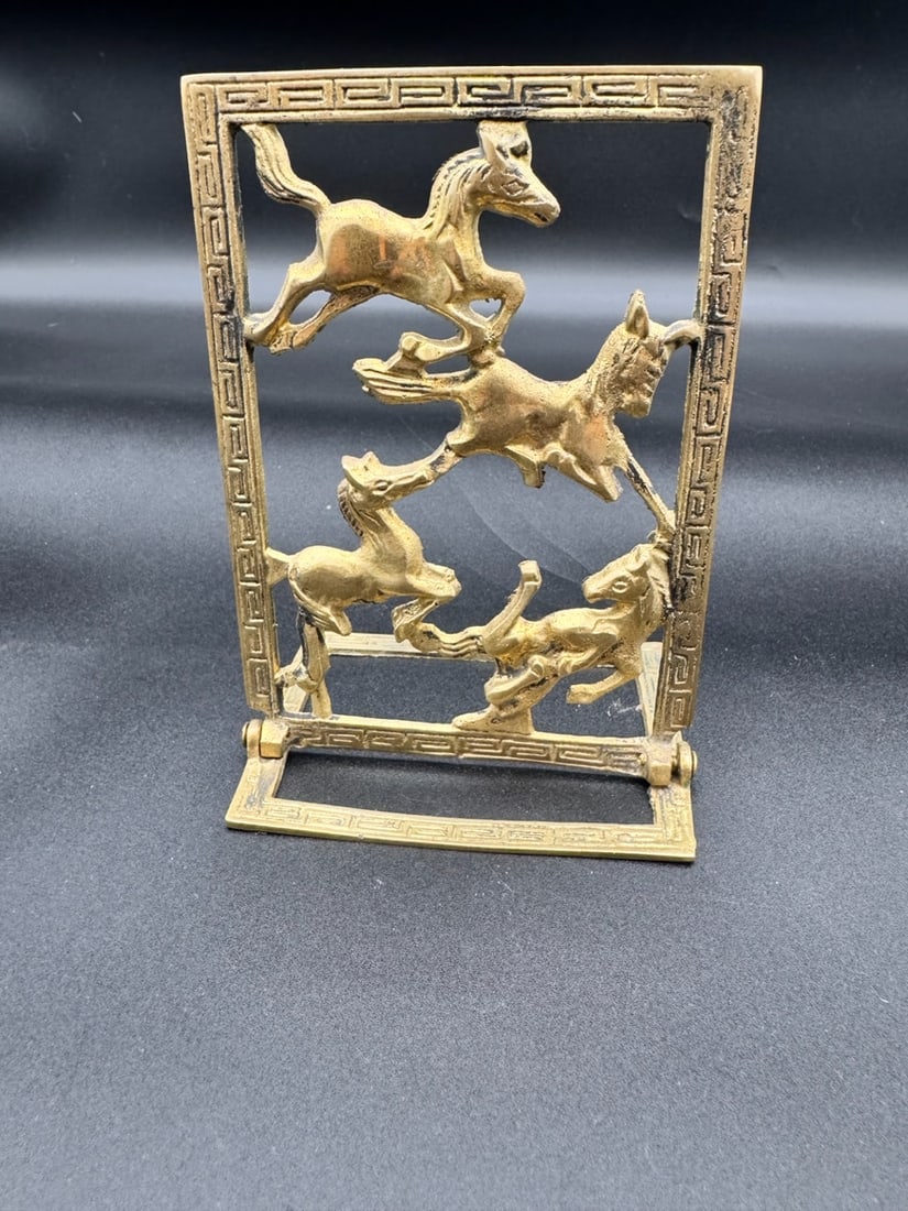 Vintage Chinoiserie Greek Brass Collapsible Bookend: Vintage Chinoiserie brass collapsible bookend featuring a cut-out design of horses framed by a Greek key pattern. These functional decorative pieces, often referred to as Chinoiserie or equestrian dec