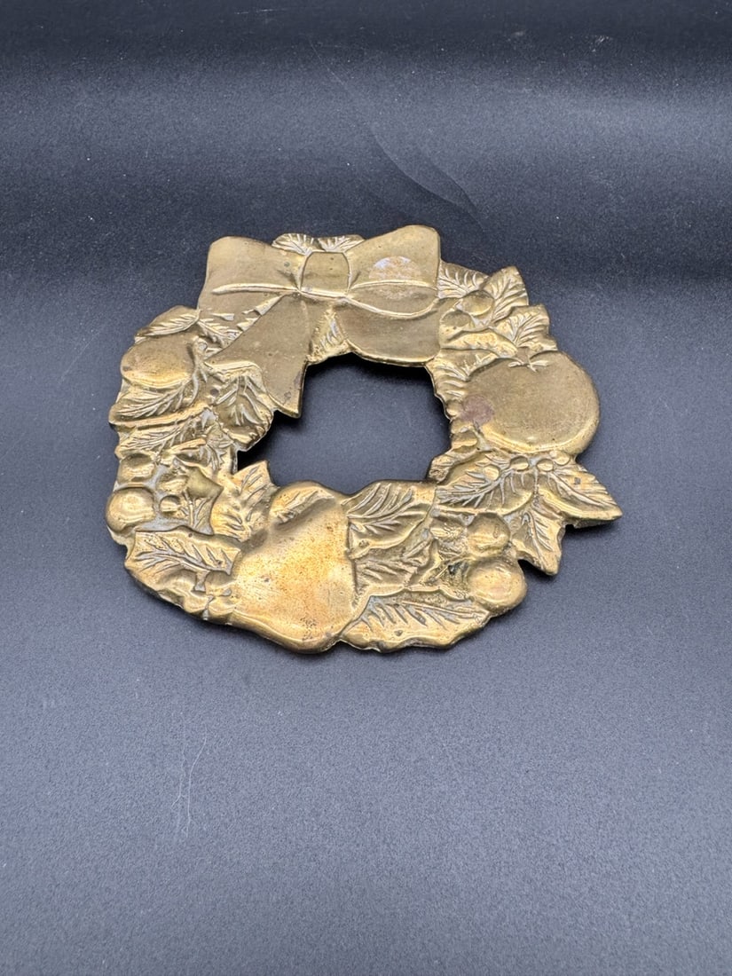 Brass Wreath Trivet: Lovely holiday wreath brass trivet featuring an intricate holiday fruit pattern including pears, apples, holly leaves and berries, topped with a bow. Designed as a decorative hot plate pad or table ce