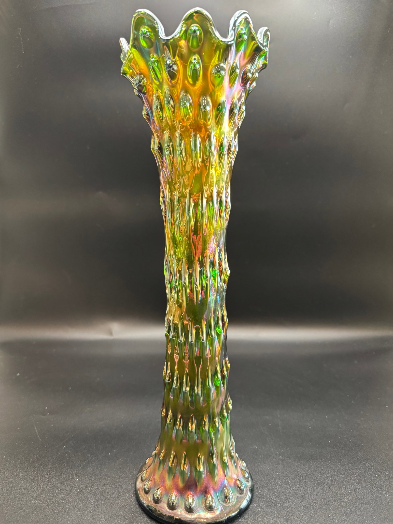 Fenton "Rustic" Carnival Glass Vase: This piece features a "Rustic" pattern, which is characterized by its bumpy or knobby texture similar to a tree trunk. It is a "swung" vase, meaning the hot glass was swung to elongate the neck, resul