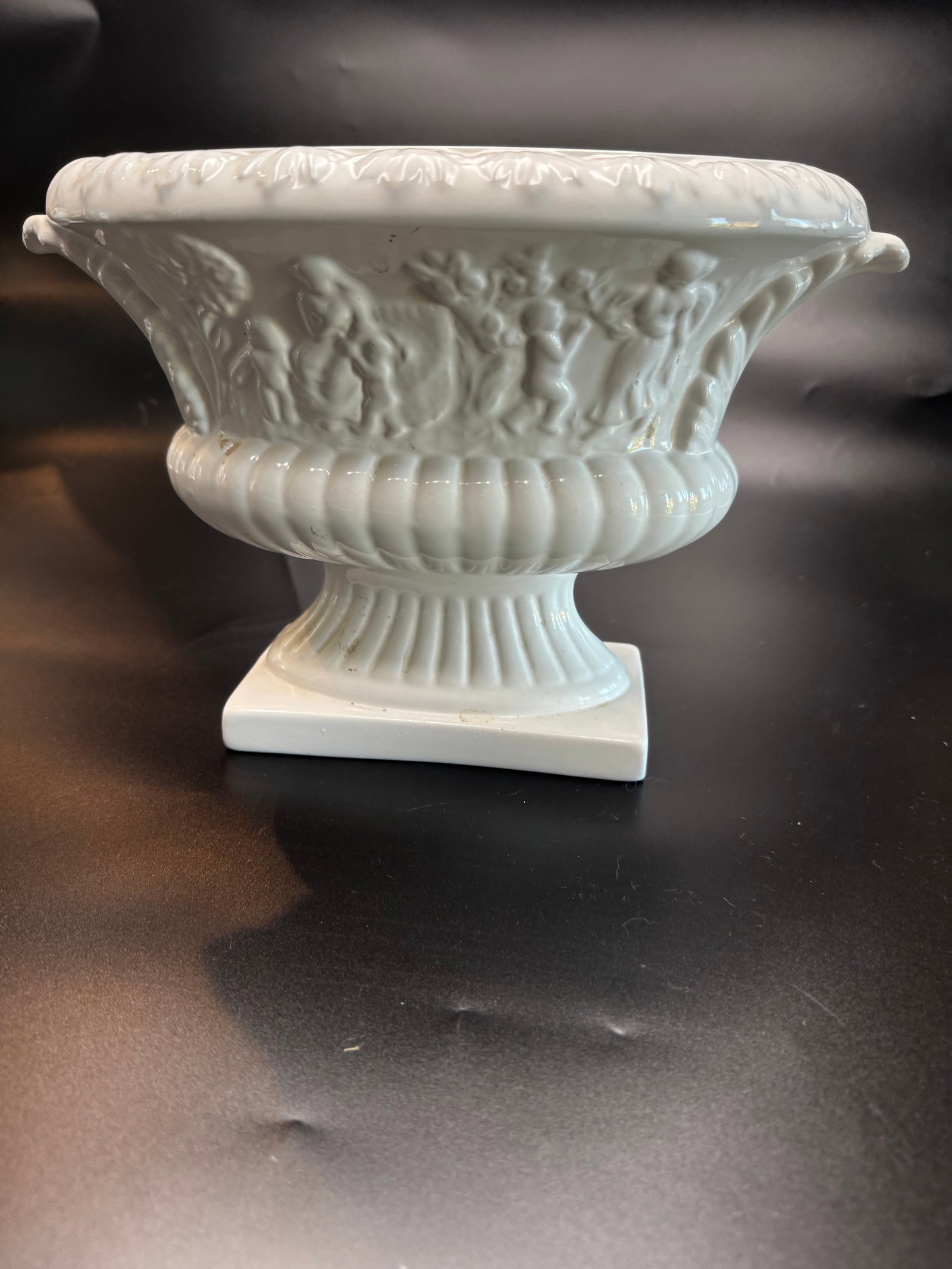 Vintage Neoclassical White Porcelain Pedestal Cachepot/Urn: This is a Neoclassical style white porcelain cachepot or urn, handmade in Portugal, featuring cherub motifs and a fluted design. Often referred to as "blanc de chine" or simply white Portuguese porcel