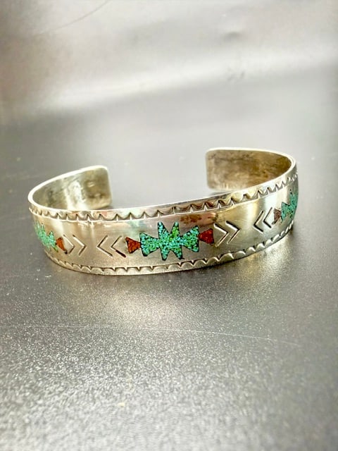 Vintage Native American Navajo Turquoise and Coral Chip Inlay Sterling Silver Cuff Bracelet: This Native American bracelet features crushed turquoise and red coral stones inlaid into a sterling silver band. The style is common in Navajo or Zuni jewelry, often dating from the mid-20th century 