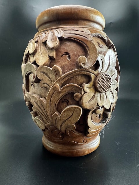 Hand Carved Floral Decorative Dark Wooden Vase/Urn: Deeply carved floral and foliate motifs covering the entire body. The urn boasts large stylized flowers resembling daisies or sunflowers. Scrollwork and acanthus-like leaves are typically common in