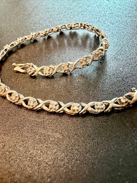 10K White Gold Tennis Bracelet with Diamond / Stone Accents: 10k white gold tennis bracelet with round diamonds / stone accents set between infinity style links. Safety clasp with figure-eight safety latch. 7 Inches long weighing 4.09 grams