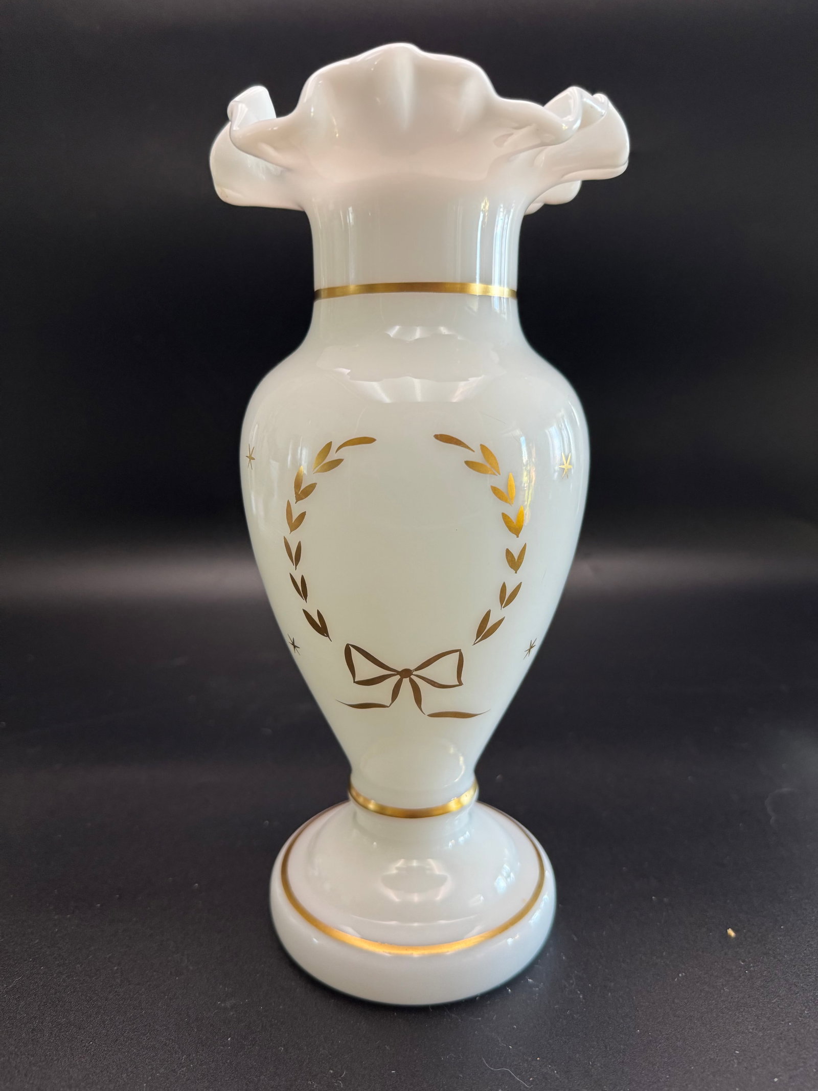 White Milk Glass Bud Vase: This white milk glass bud vase features a ruffled rim and delicate gilded laurel wreath decorations. Based on the ruffled shape, it is likely dating from between 1940 and 1960. Ruffled crumpled rim