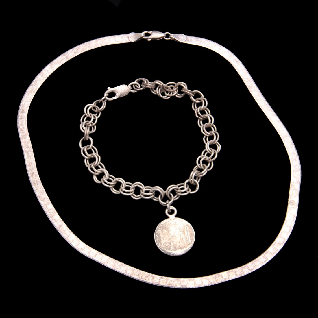 Sterling Silver Charm Bracelet and Herringbone Necklace: A vintage 8" sterling silver charm bracelet with a single charm that has inscribed initials and dates to both sides, charm and bracelet both marked 925. The herringbone necklace has a greek design to 