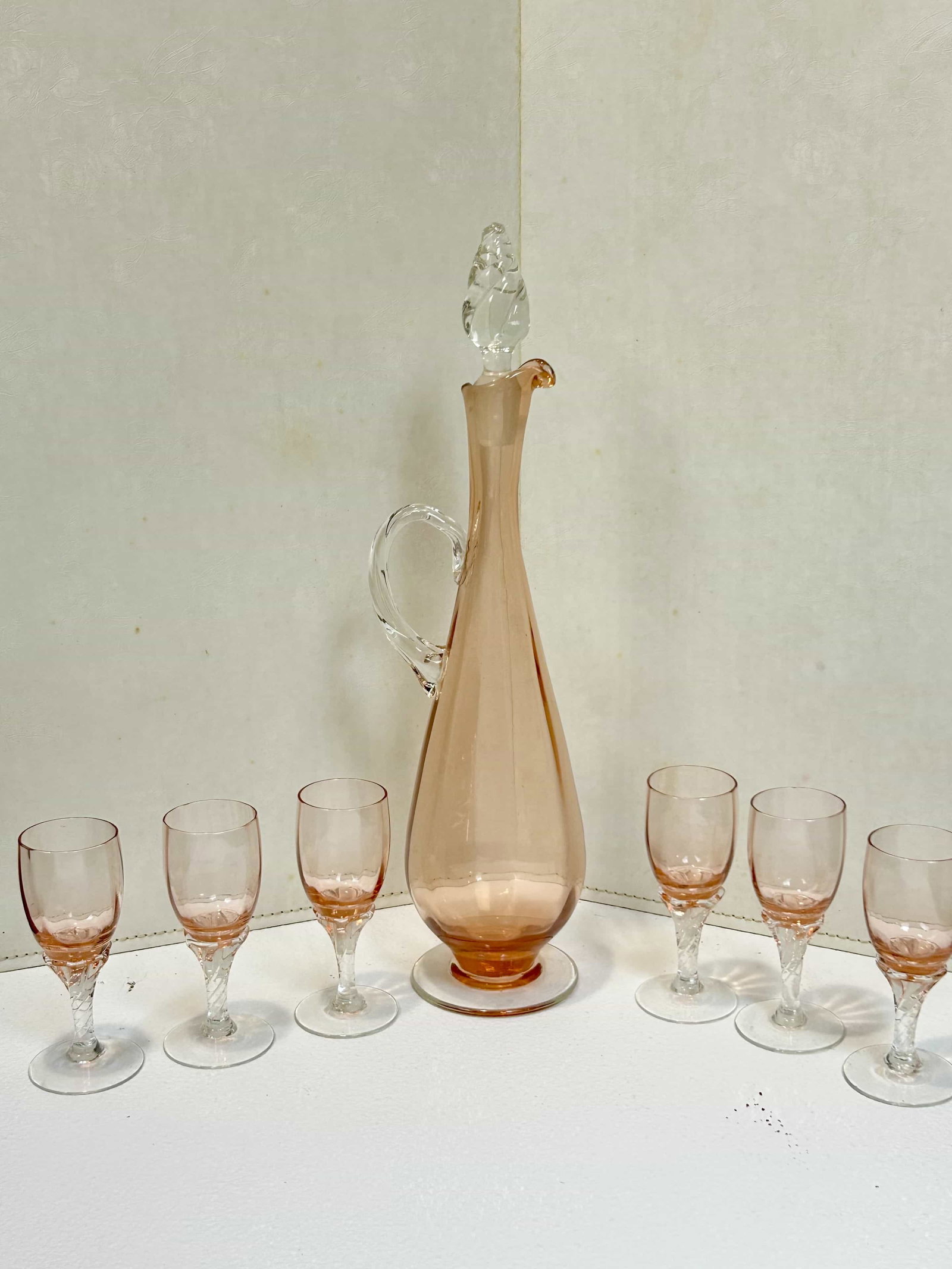 Vintage Peach Glass Decanter w/ 6 Stemmed Glasses: Vintage Mid-Century peach glass decanter set w/ 6 stemmed glasses. Decanter measures 15" tall, glasses measure 4.5" tall. Condition is good, other than a small chip on the bottom side of the stopper (