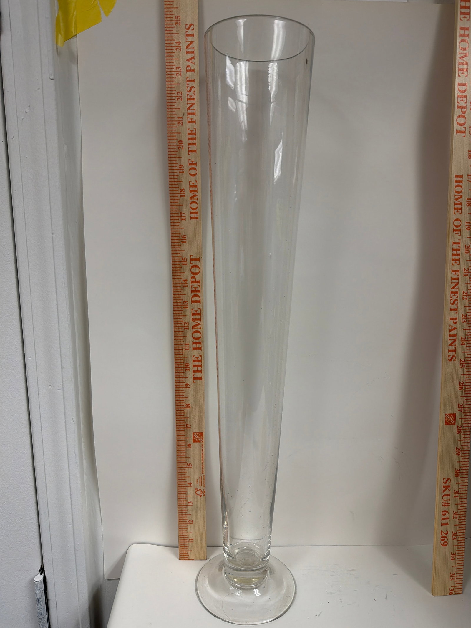 24" Tall Clear Glass Trumpet Pilsner Vase – Elegant Footed Centerpiece: The item in the selected region is a clear glass trumpet pilsner vase, which features a tall, tapered conical shape resting on a flat circular footed base. It stands approximately 24 inches tall (or