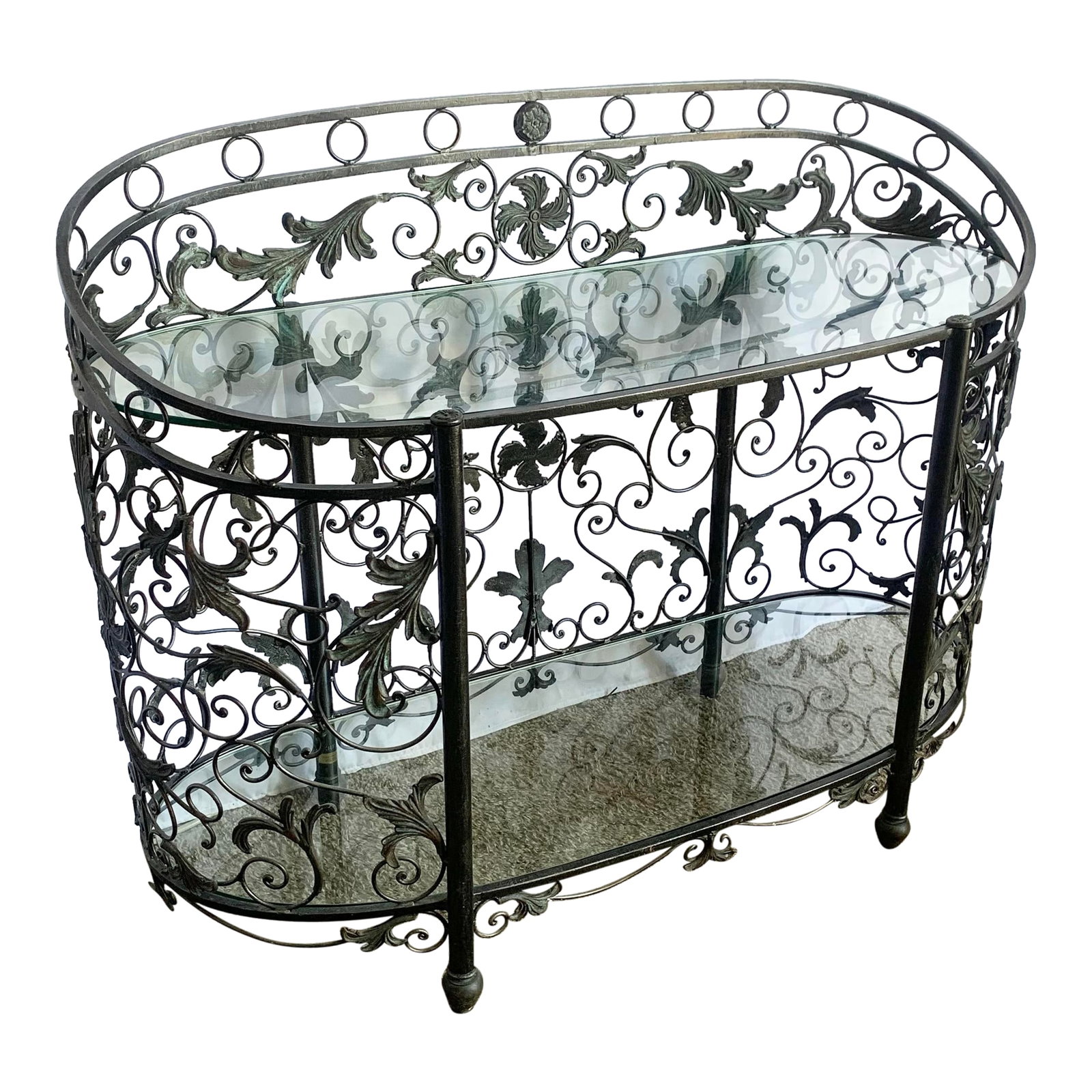 Vintage Wrought Iron Oval Two Tier Glass Top Console Table by Maitland Smith: Ornate and timeless, this Maitland Smith-style console table features hand-forged wrought iron in a gracefully rounded silhouette. The botanical scrollwork and verdigris-accented foliage add depth
