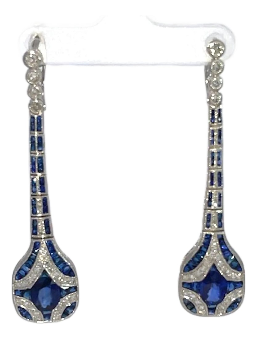 1960s Pair of Art Deco Sapphire and Diamond Drop Earrings: These breathtaking Art Deco earrings exudes timeless elegance with its striking long drop design set in lustrous Platinum. Deep, vivid blue sapphires take center stage, arranged in precise geometric