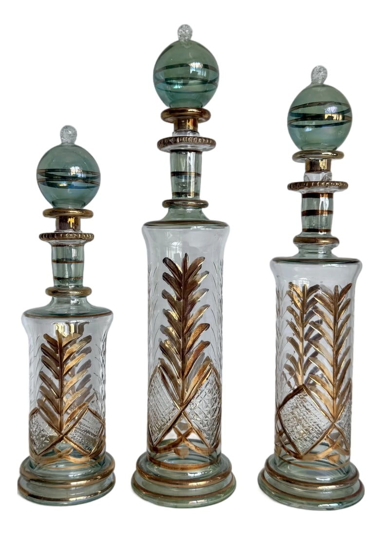 Vintage Set of 3 Hand-Blown Glass Perfume Apothecary Bottles and Stoppers: This decorative set of three Egyptian hand-blown glass bottles in varying heights, was likely produced in the later mid-century. They feature pale aqua tinted glass with applied gold botanical