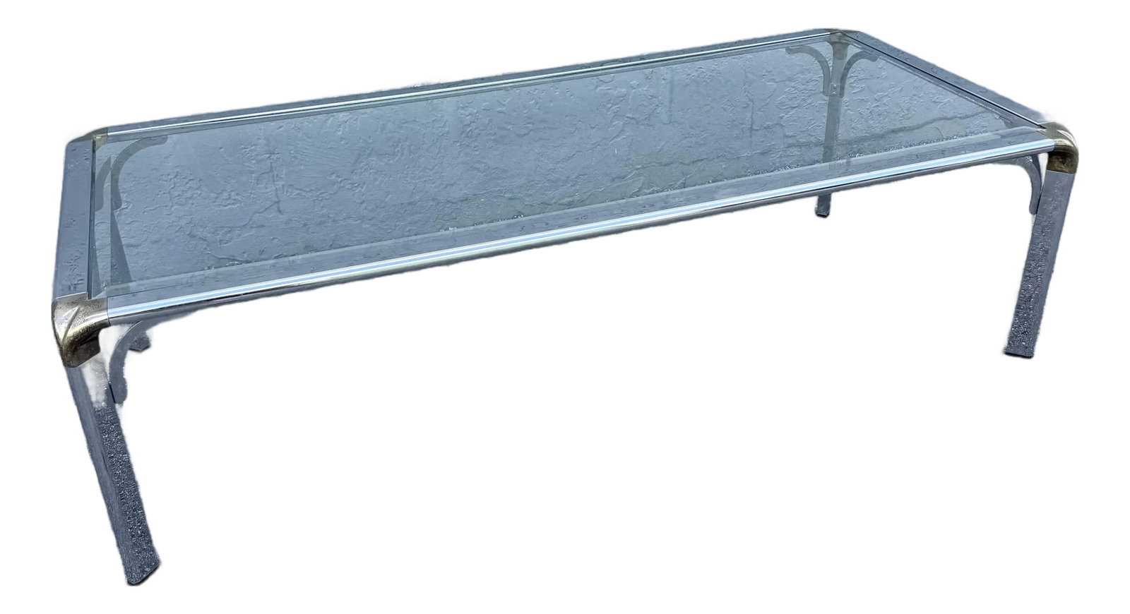 Hollywood Regency Golden Chrome Coffee Table: A refined Hollywood Regency coffee table blending glamorous materials with sleek modern lines. The elongated silhouette features a clear glass top framed by polished chrome with subtle golden corner