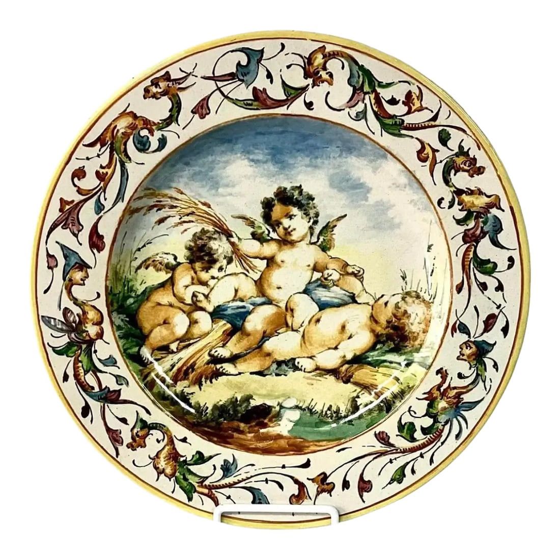 19th Century Italian Majolica Charger: 19th century hand painted Italian charger featuring three cherubs interacting with another lying on a bed of wheat stalks under a scenic skyscape. Beautiful yellow, blue and green color palette.
