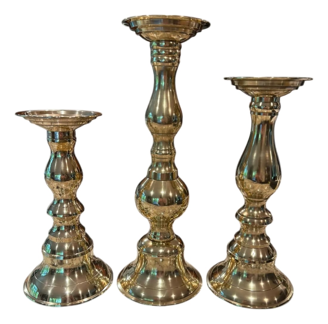 Polished Brass Candlesticks Set of 3: Offering a polished set of three polished brass candlestick holders. Each holder offers a unique central columns that is turned and shaped, featuring a series of bulbous swells and narrower sections, 