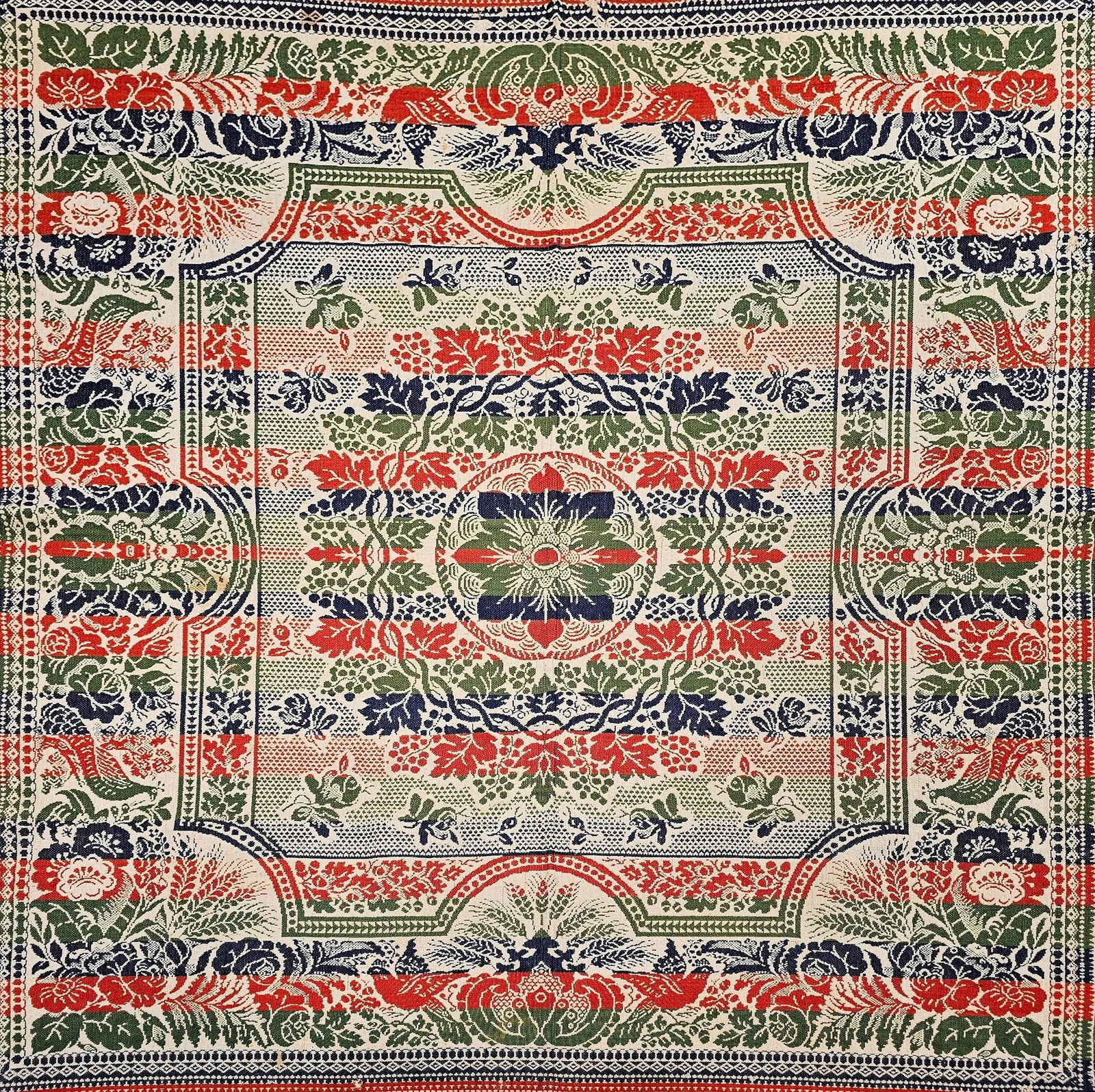 Mid-19th Century American Jacquard Coverlet With Floral & Bird Design: This mid-19th century American coverlet is a stunning handwoven textile created on a Jacquard loom, featuring a rich palette of blue, red, green, and natural ivory. At its center is a floral medallion