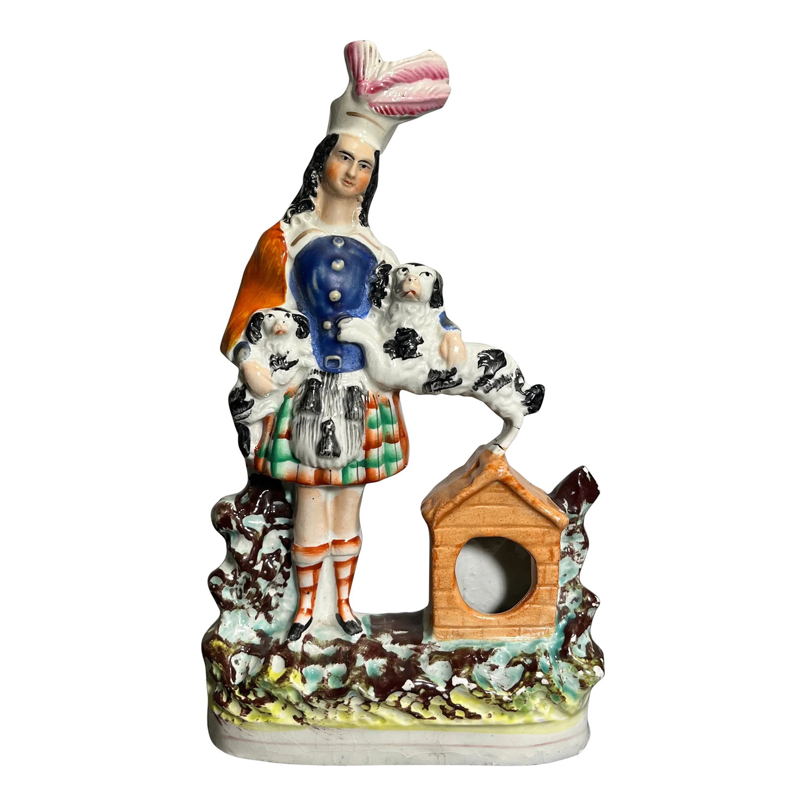 Antique Staffordshire Figurine, England: Portraying a man with two dogs, one in his arms and the other standing atop his own dog house to get some attention. Good vibrant colors, particularly the orange and green glaze on kilt and pink tone 