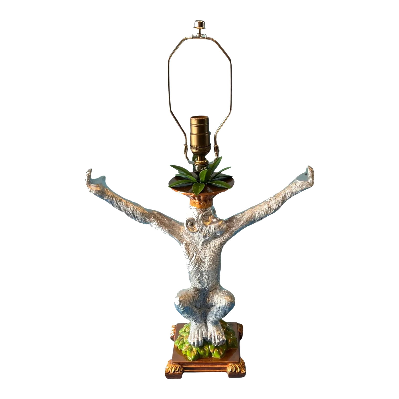 Vintage Chrome Tone Chimpanzee Table Lamp: This whimsical table lamp features a delightful chimpanzee perched atop a lush pile of vibrant green leaves. The chimp's expressive face is turned to the left, giving it a curious, alert appearance, a