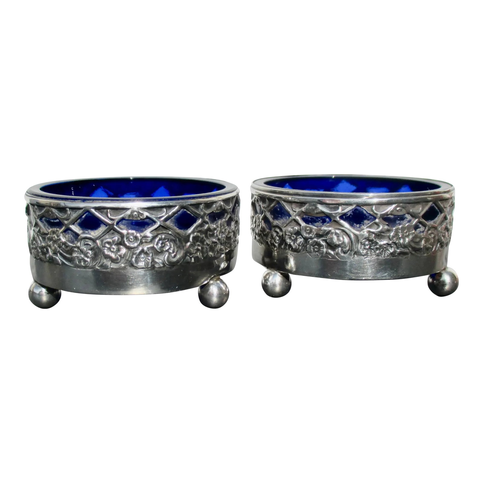 Sterling Silver Salt Cellars- A Pair of 2: Sterling Silver salts with cobalt blue glass liners. Mid-century openwork silver mounts. Deep blue cobalt glass hallmarked sterling to the bottom rim"”Beaux Arts motif with ball feet. INV 75