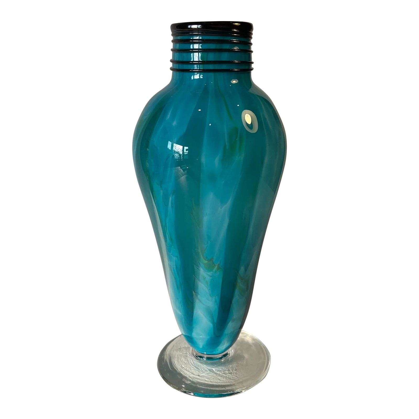 Art Glass Blue Teal Pedestal Vase With Swirl Pattern: This art glass vase was skillfully hand-blown using shades of blue and teal glass, creating captivating vertical swirls along its body. Cobalt blue loops of glass surround the cylindrical neck and